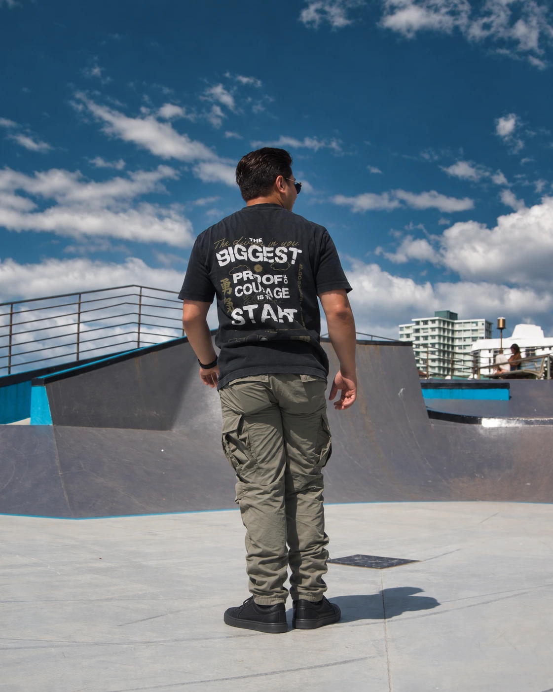 Ricardo in a BIGGEST graphic tee, olive trousers and black sneakers at a skatepark