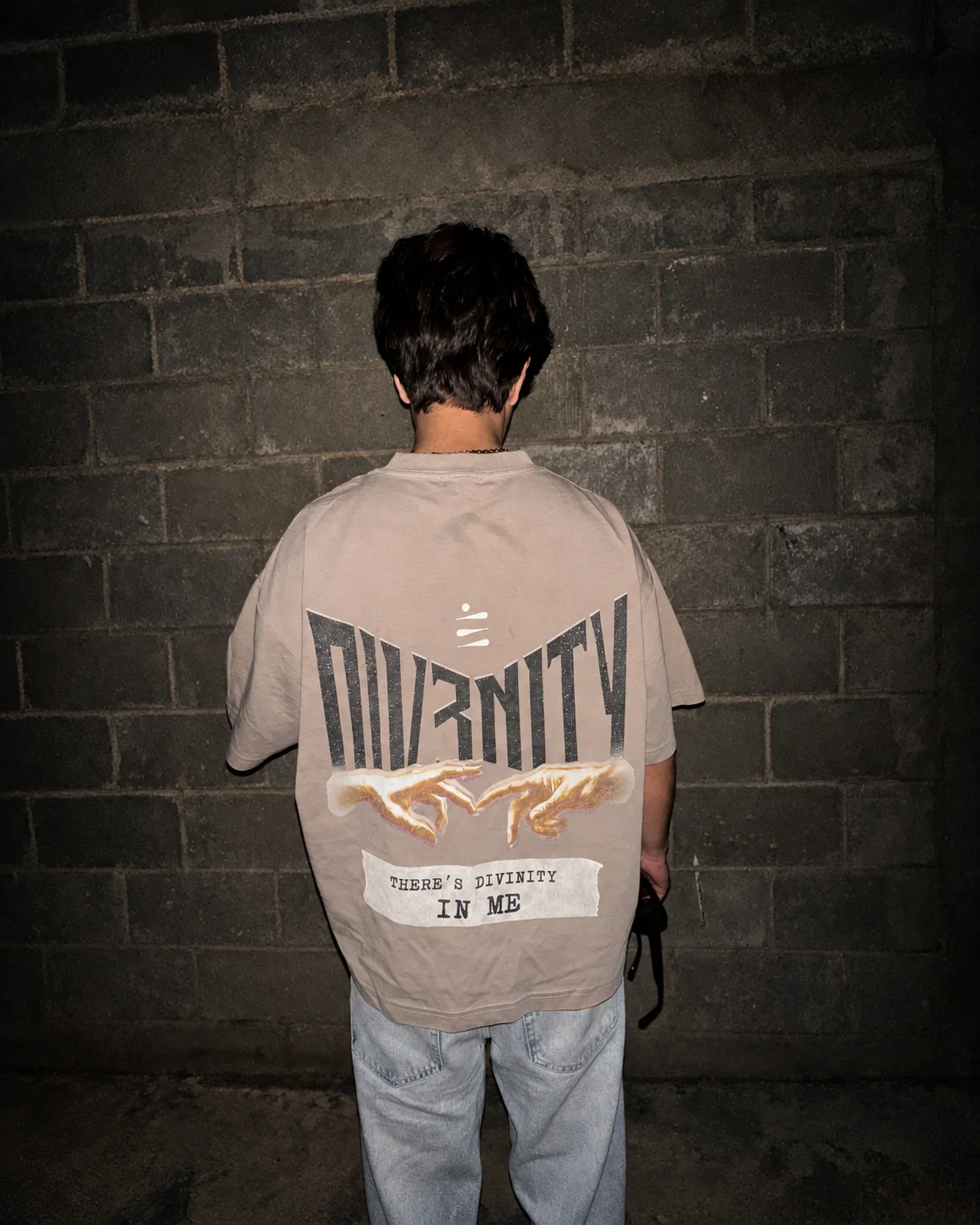 Back of a DIV3NITY T-shirt against a concrete wall